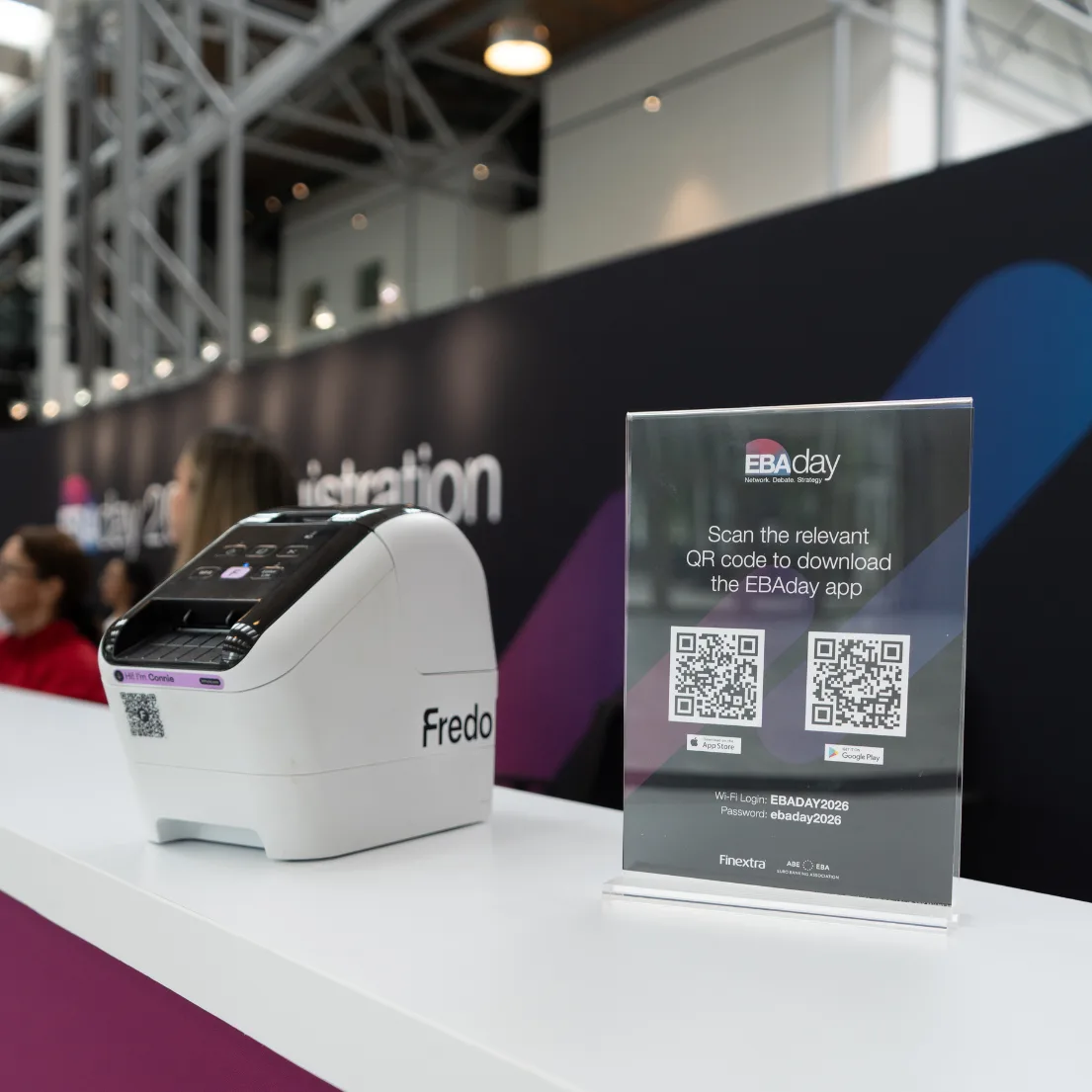 Fredo badge printer on an event counter beside an EBAday QR-code sign